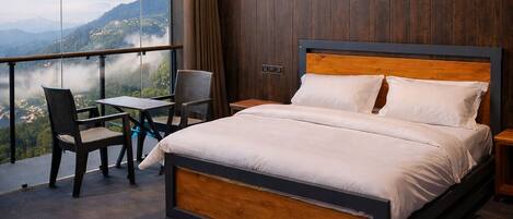 A bedroom with a large bed, a ceiling fan, a view of the mountains, and a balcony with chairs.