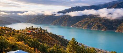 A mountain landscape with a lake, trees, and a building with a blue roof.