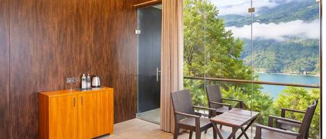 A balcony with a table and chairs, a wooden cabinet, and a view of a lake and mountains.