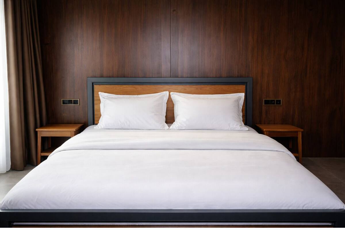 A modern bedroom with a wooden headboard, two white pillows, a large bed, and two bedside tables.