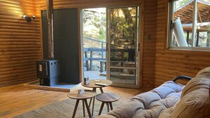 A cozy log cabin interior with a sofa, two small tables, a fireplace, and a sliding glass door leading to an outdoor deck.