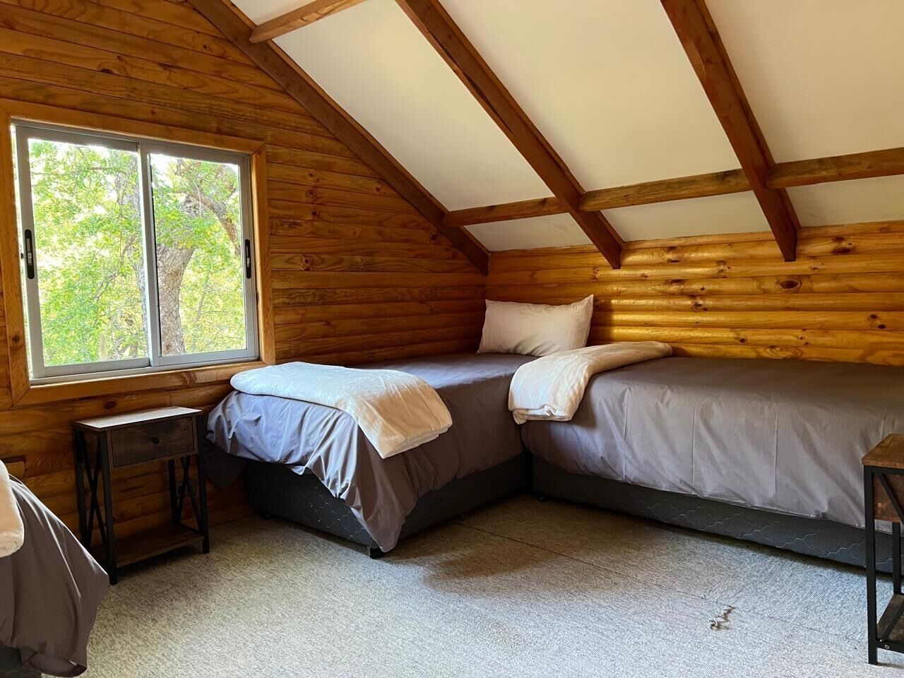 A small, cozy room with a sloped ceiling, two beds, a window, and a small table.