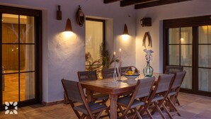 A dining area with a wooden table and chairs, candles, a vase with flowers, and a bowl of fruit. - Villa HARMONIA by Abahana Villas (Teulada)