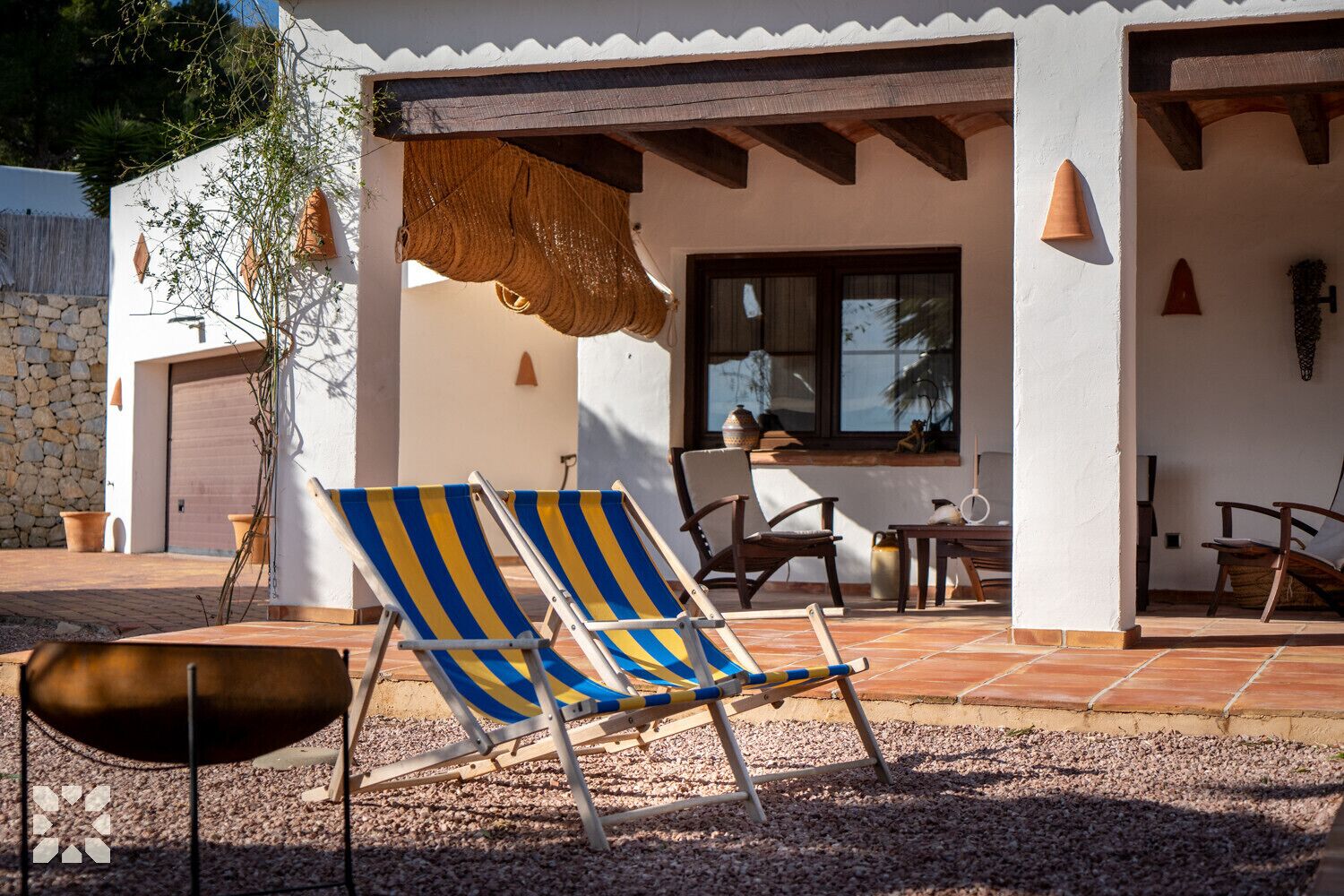 Un patio con dos sillones a rayas, una mesa y una parrilla.