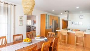 A modern kitchen with wooden cabinets, a central island, and a dining area with a table set for two. - Villa HARMONIA by Abahana Villas (Teulada)