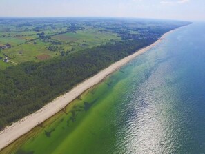 An aerial view of a coastal area with a long sandy beach and a forested area adjacent to a greenish-blue sea. - Holiday Home in Mielenko Near Seaside Beach (Mielno)