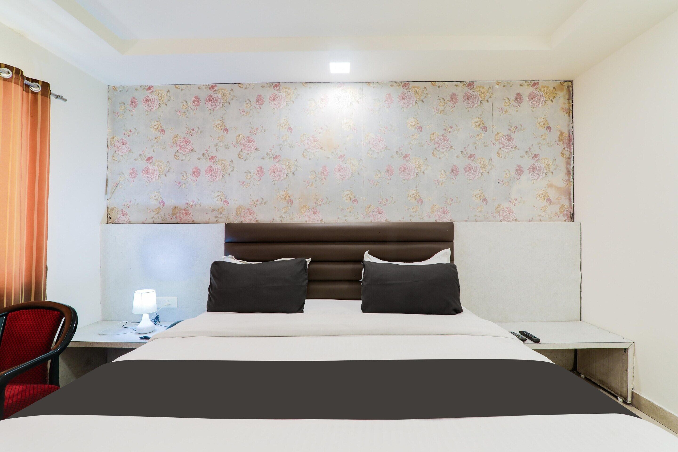 A hotel room with a bed, a desk with a lamp, a chair, and a floral-patterned headboard.