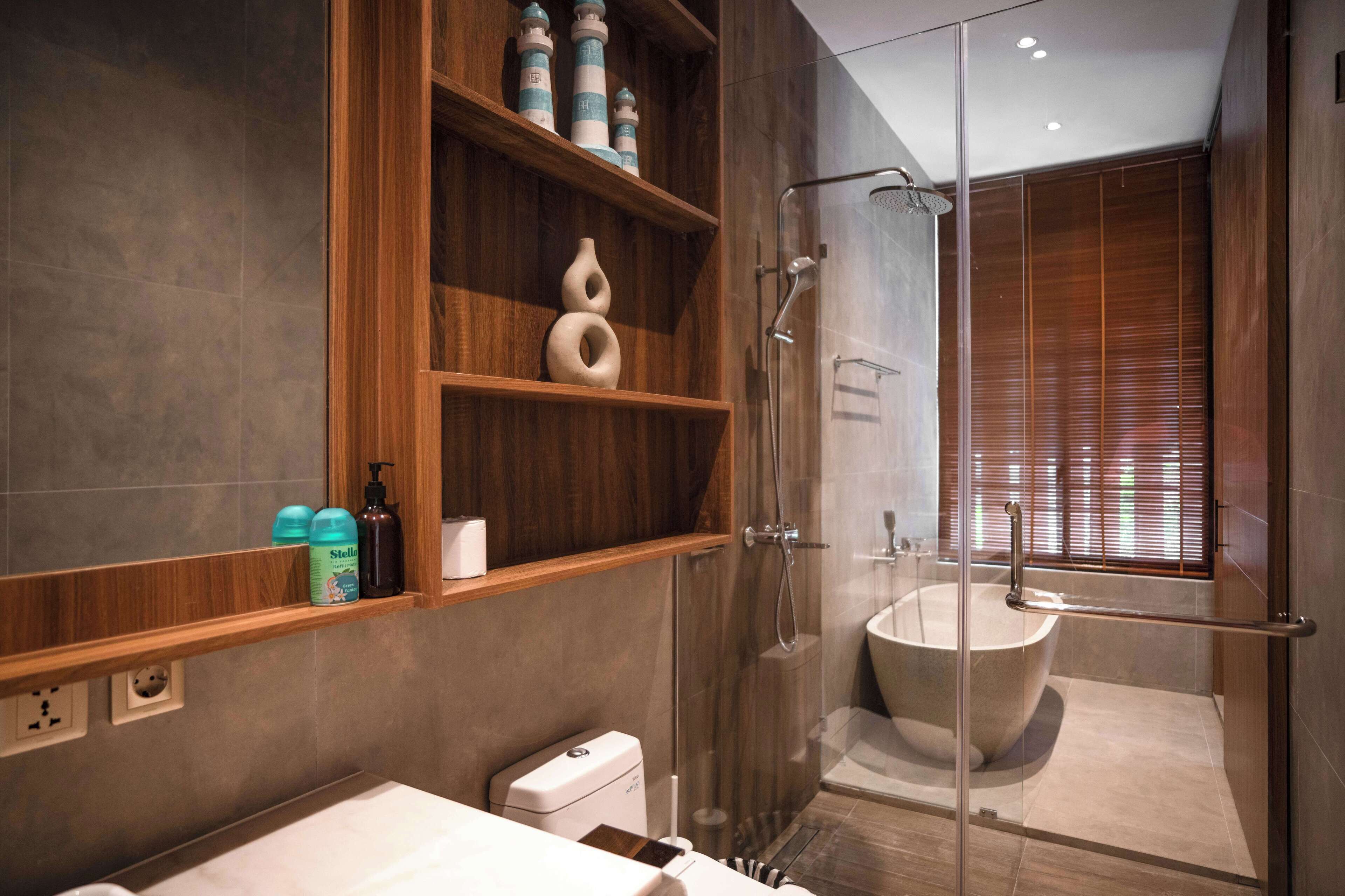 Une salle de bain moderne dotée d’une douche à parois de verre, d’une baignoire sur pieds et d’étagères en bois où sont rangés les articles de toilette.
