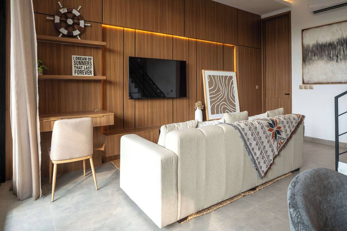 A modern living room with a sofa, a TV, wooden paneling, and a desk.