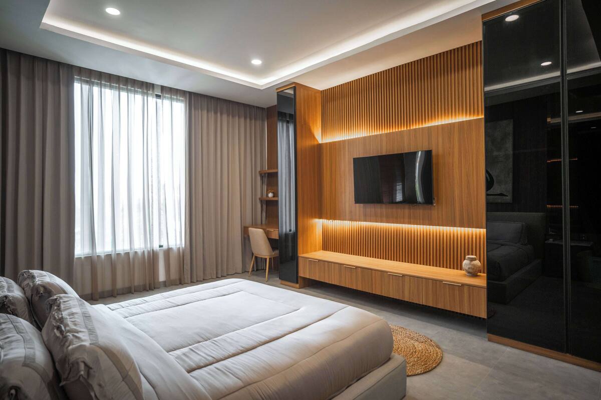 A modern bedroom with a large bed, a TV mounted on a wooden wall, and a sliding glass door closet.