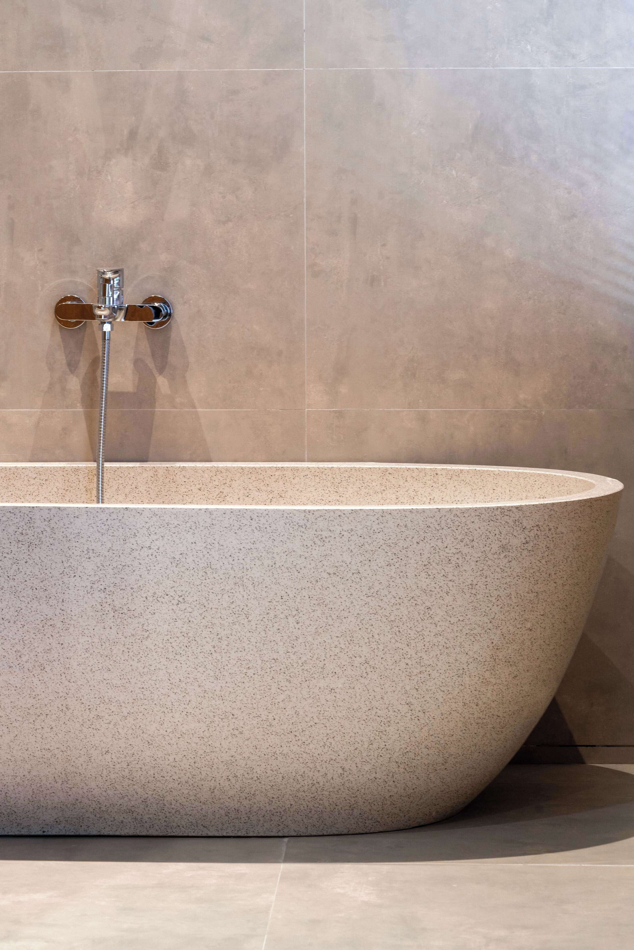 A freestanding bathtub with a modern design, positioned against a tiled wall.