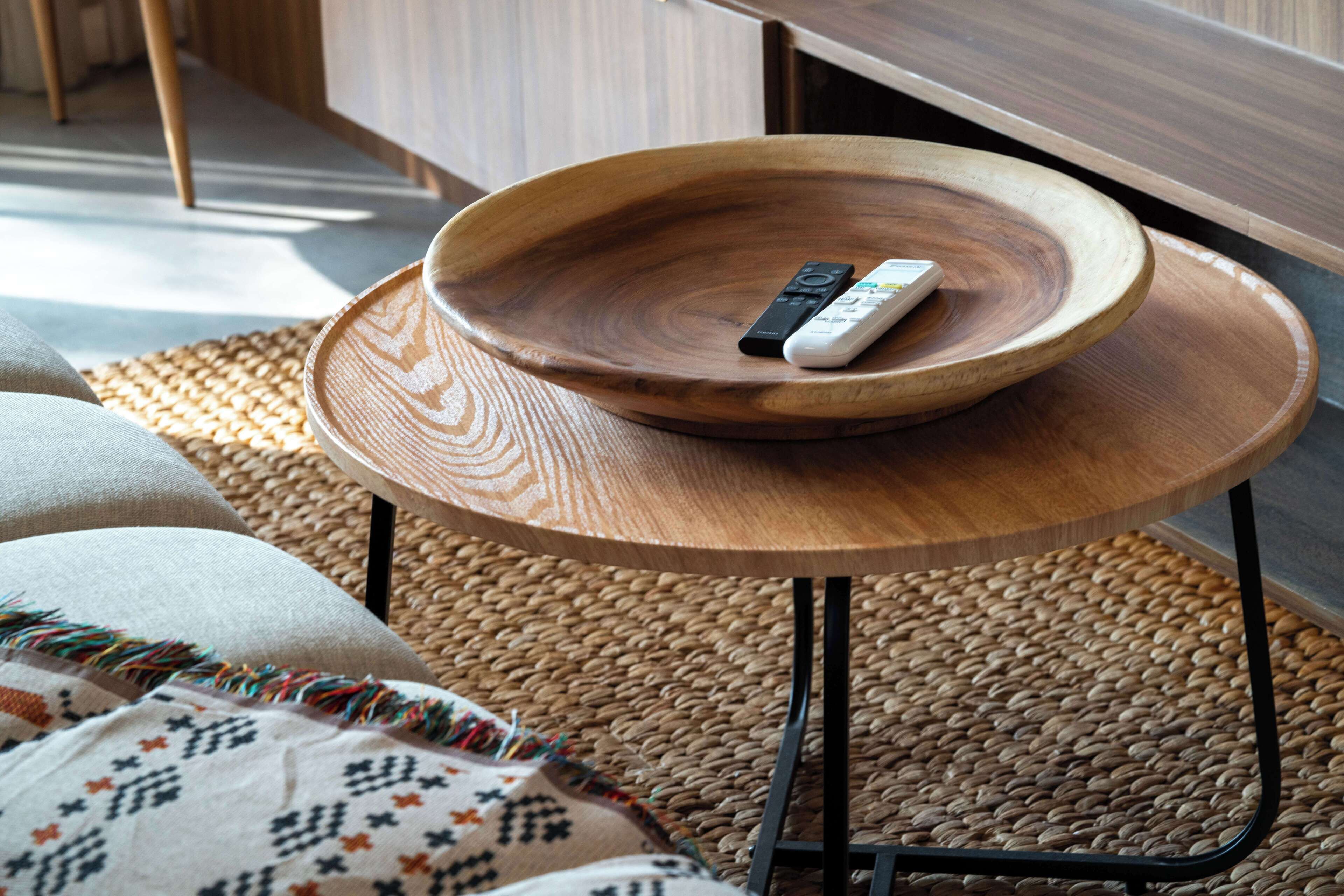 A wooden bowl on a round table with a remote control inside.