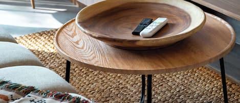 A wooden bowl on a round table with a remote control inside.