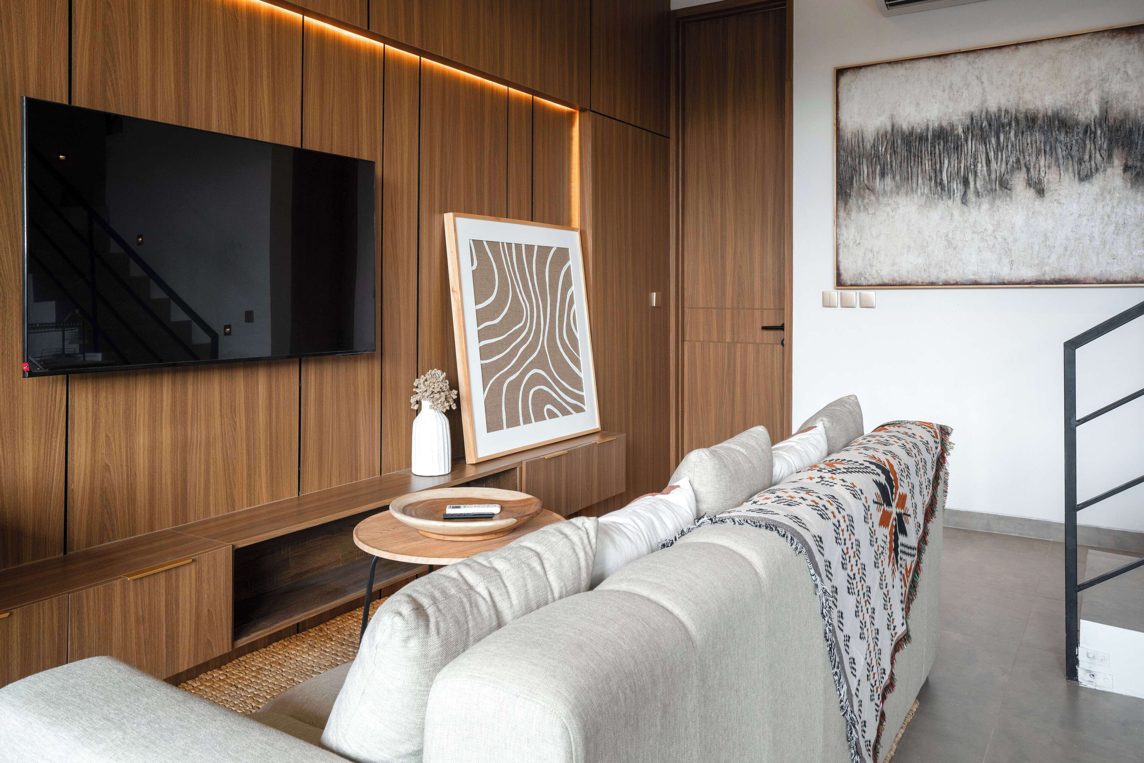 Una sala moderna con un televisor de pantalla plana grande, paneles de madera, un sofá, una mesita redonda y una obra de arte abstracta enmarcada.