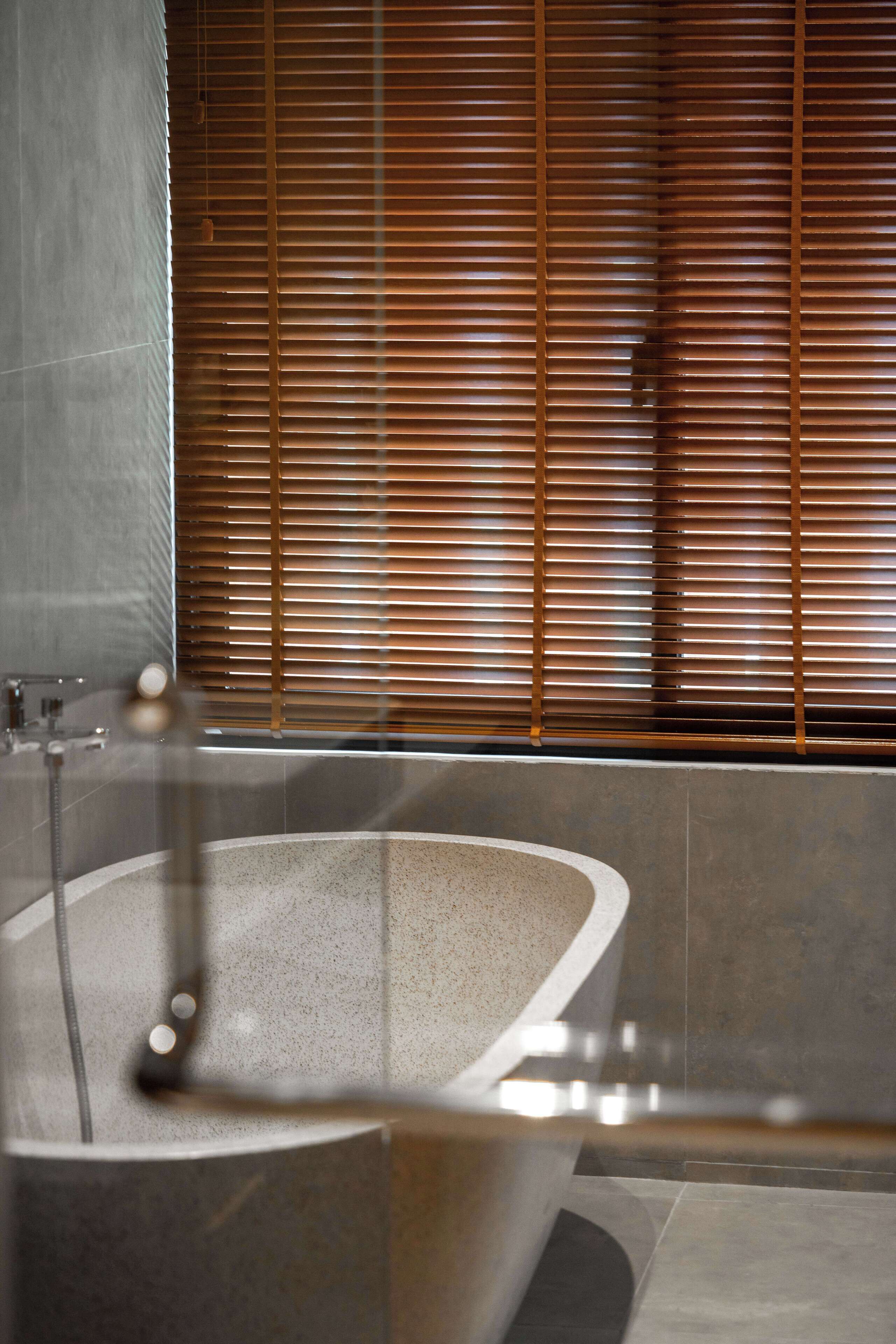 Une salle de bain moderne avec une baignoire sur pieds, des murs carrelés et des stores en bois.