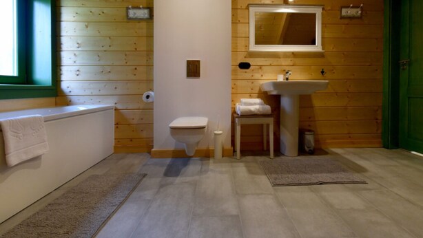 Une salle de bain aux murs lambrissés, équipée de toilettes, d’un lavabo et d’un miroir placé au-dessus.