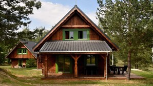 Une cabane en bois avec un toit en pente, une véranda avec des sièges et une grande fenêtre.
