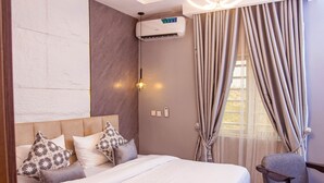 A hotel room with a bed, a chair, an air conditioning unit, and a window with curtains. - TM Luxe Stays Apartment  (Ibadan)