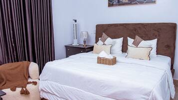 Una cama bien hecha con ropa blanca, un cabecero marrón y almohadones decorativos.