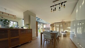 A modern kitchen with wooden cabinets, a dining area with a table and chairs, and a large window allowing natural light. - Design villa with glass roof and parquet flooring, garden and fitness center near downtown (Montpellier)