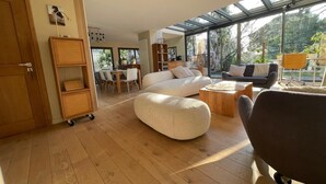 A modern living room with a large sectional sofa, a round coffee table, and a dining area with a wooden table and chairs. - Design villa with glass roof and parquet flooring, garden and fitness center near downtown (Montpellier)
