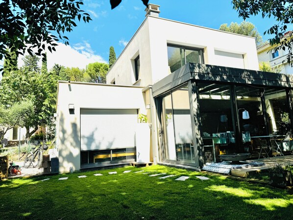 A modern two-story house with a garage, a covered patio area, and a well-maintained lawn. - Design villa with glass roof and parquet flooring, garden and fitness center near downtown (Montpellier)