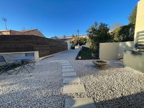A gravel pathway leading to a seating area with a table and chairs, surrounded by a wooden fence and a potted plant. - Design villa with glass roof and parquet flooring, garden and fitness center near downtown (Montpellier)
