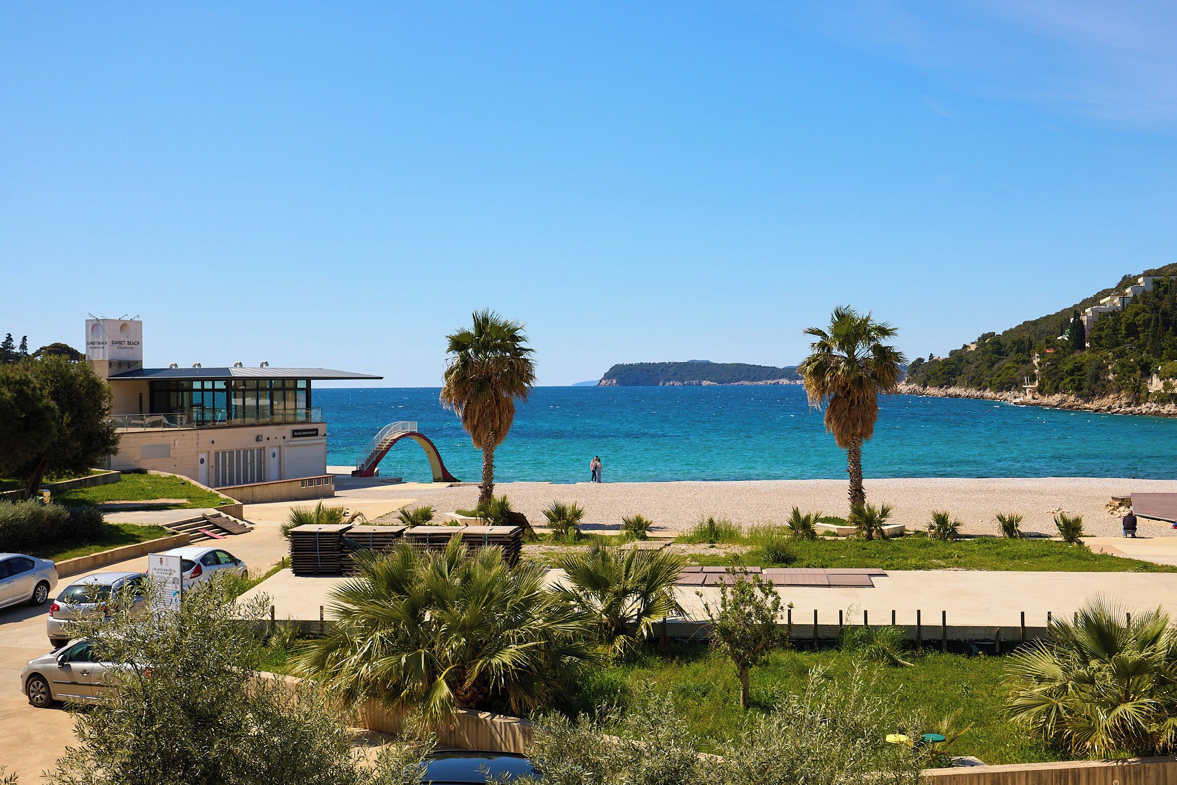 Un hotel costero de arquitectura moderna, con vista a la playa y un estacionamiento con varios coches.