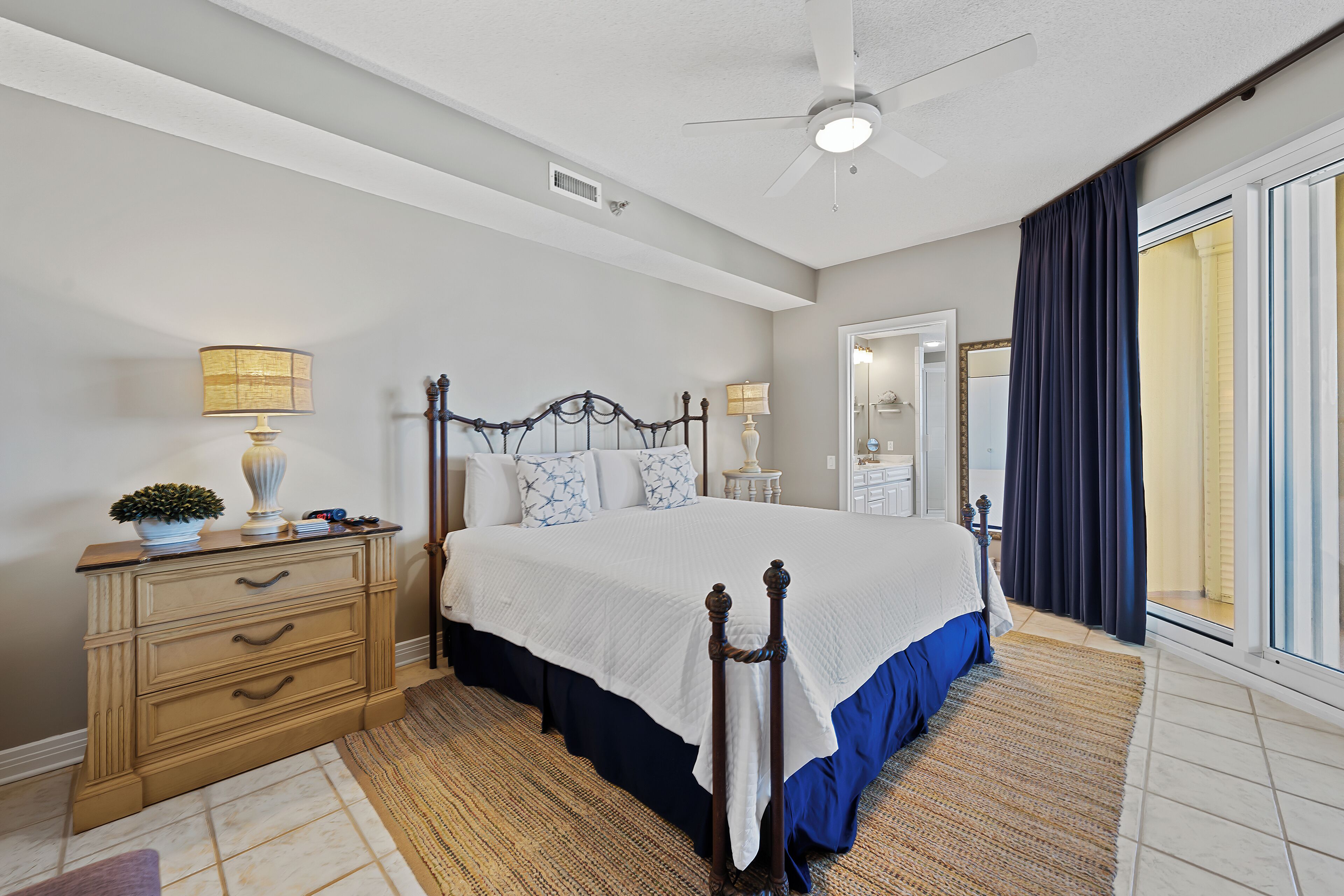 A bedroom with a bed, a dresser, a ceiling fan, and a view of the outside.