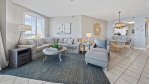 A spacious living room with a grey sofa, a coffee table, and a dining area with a table and chairs. - Beach Colony W7C - Covered Parking Included (Perdido Key)