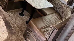 A cozy RV interior with a marble-top table, brown cushioned seating, and patterned curtains. - RV in charming Forks with WiFi, AC. Happy travel and 1 block from Bella’s house! (Forks)