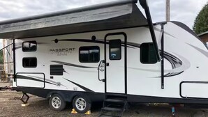A white recreational vehicle with a large awning, labeled "Passport UltraLite," featuring a ramp for easy access and a small window on the side. - RV in charming Forks with WiFi, AC. Happy travel and 1 block from Bella’s house! (Forks)