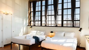 A hotel room with two beds, a large window with curtains, a door, and a nightstand with a lamp. - Sosuite | 2BR Apt w W/D, Gym, On-Site Restaurant (Philadelphia)