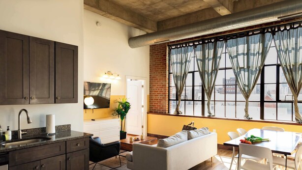 A modern kitchen with dark cabinets, a sink, and a dining area with a white table and chairs. - Sosuite | 2BR Apt w W/D, Gym, On-Site Restaurant (Philadelphia)