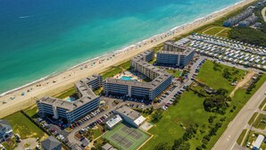 Un hotel frente al mar con varias construcciones, una playa y un estacionamiento.