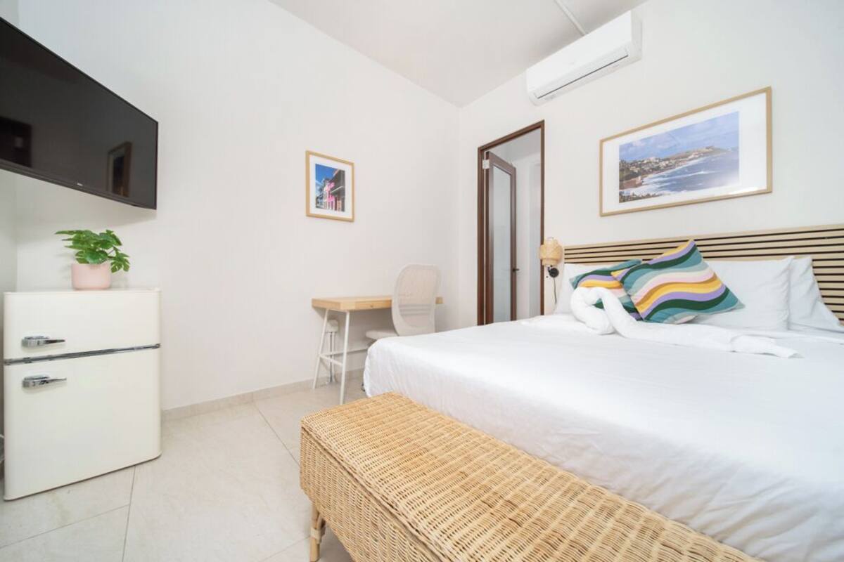 Un dormitorio con cama, escritorio, silla, televisor y una planta pequeña.