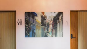 En gang med et stort billede af farverige bygninger, en dør med kode lås og et skilt til toilet.
