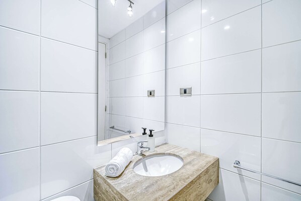Un baño moderno con azulejos blancos, un lavabo de mármol, un espejo y una toalla.