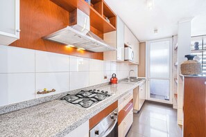 Una cocina moderna con armarios blancos, encimera de granito, estufa a gas y estanterías de madera.