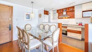 A modern kitchen with wooden cabinets, a glass dining table, and a red kettle.