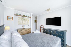 Un dormitorio con cama, cómoda, mapa y televisor montado en la pared.