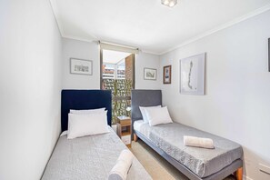 A room with two beds, a small table, and a view through an open door. - Castano Home - AC & Estacionamiento en la Ciudad (Las Condes)