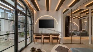 A modern living room with a large window, a flat-screen TV mounted on the wall, a sofa, and a coffee table. - Elounda Riviera Villa (Elounda)