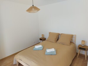 Une chambre à coucher comprenant un lit, deux tables de chevet, un luminaire suspendu et une prise électrique murale.