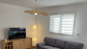 Una sala de estar con un sofá gris, un mueble de madera, un televisor y una lámpara de pie.