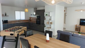 Una cocina moderna con mesa de fútbol, un comedor con mesa y sillas, y una sala de estar con sofá y televisor.
