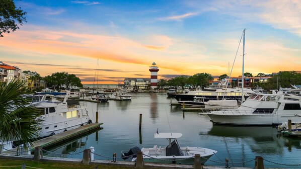 A marina with boats docked, a lighthouse in the background, and buildings along the waterfront.