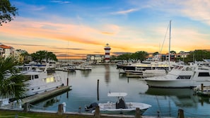 Una marina con barcos amarrados, un faro al fondo y edificios a lo largo del paseo marítimo.