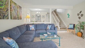A living room with a sectional sofa, a glass coffee table, a staircase, and a dining area in the background. - Waterfront Sea Pines Villa | 3 Private Suites, Balconies, Dock Access (Hilton Head Island)