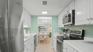 A kitchen with white cabinets, stainless steel appliances, and a view into the dining area. - Waterfront Sea Pines Villa | 3 Private Suites, Balconies, Dock Access (Hilton Head Island)